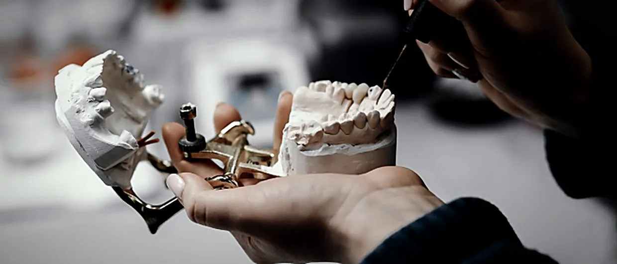 Prothésiste dentaire ajustant un modèle sur articulateur dans l'atelier du laboratoire
